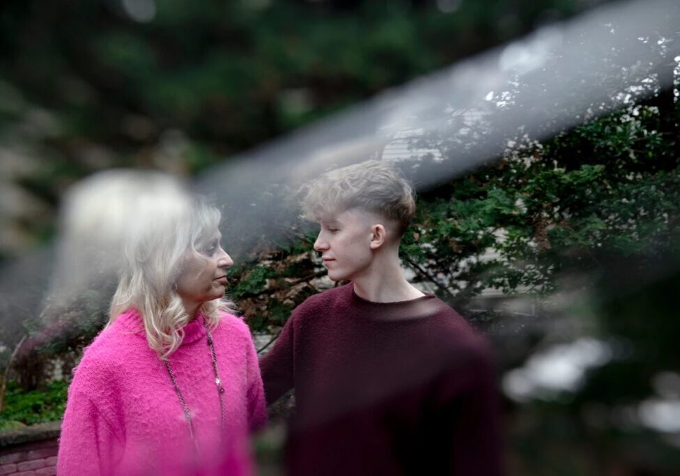 a boy and a woman standing with trees around